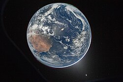 Photograph of Earth taken by the Artemis II mission. Two auroras lie in the top right and bottom left and zodiacal light surrounding the bottom right of the disc. From a top-down view, the arid region of Northwest Africa appears below the Iberian peninsula, where city lights are most visible, and the eastern coast of South America is faintly seen across the Atlantic Ocean.