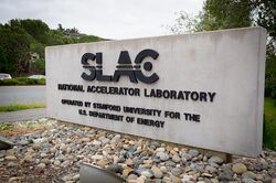 A concrete monument sign reads "SLAC National Accelerator Laboratory: Operated by Stanford University for the U.S. Department of Energy".