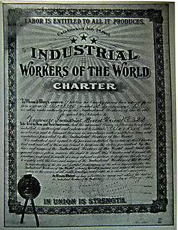 Framed, formal document featuring various IWW themes, cursive body text, hand-filled forms and a stamped seal.