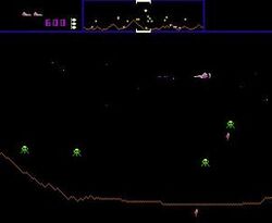 A horizontal rectangular video game screenshot that is a digital representation of a planet surface. A white, triangular spaceship in the upper right corner battles green alien enemies. The top of the screen features a banner that displays icons, numbers, and a miniature version of the landscape.