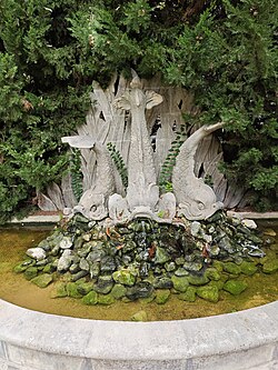 Carved stone fish fountain with water flowing over moss-covered rocks in Aix-en-Provence