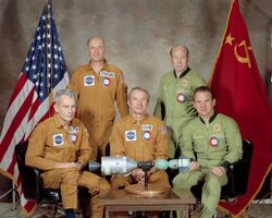 the five crew members of ASTP sitting around a miniature model of their spacecraft