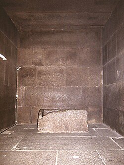 Square chamber constructed out of red granite blocks with a granite sarcophagus in the center.