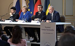 Quatre dirigeants installés à une table devant un parterre d'auditeurs, avec les drapeaux de leurs pays respectifs en arrière-plan.