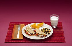 Dinner plate with fish tacos, oranges, corn, and beans, next to a cup of milk