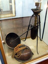 A glass display case holds a mechanical device with a lever arm, plus two metal hemispheres attached to draw ropes.