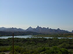 View of a wide river flowing through a forested area, with jagged mountains in the background