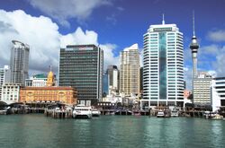 Boats docked in blue-green water. Plate glass skyscrapers rising up in the background.