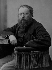 Black-and-white photo of a bearded man with glasses wearing a dark coat