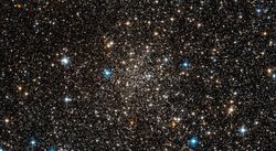 A loose scattering of small dull white dots on a black background with a few brighter coloured stars