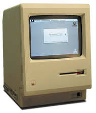 A beige, boxy computer with a small black and white screen showing a window and desktop with icons.