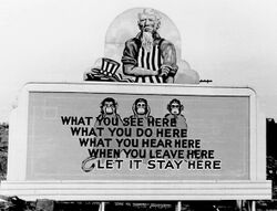 Uncle Sam has removed his hat and is rolling up his sleeves. On the wall in front of him are three monkeys and the slogan: What you see here/ What you do here/ What you hear here/ When you leave here/ Let it stay here.