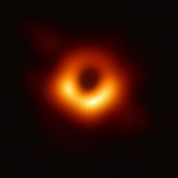 A black spot, center, surrounded by a doughnut-shaped orange-yellow ring with the blackness of empty space in the background