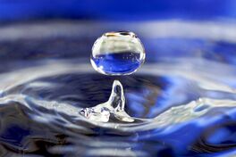 A drop of water falling towards water in a glass