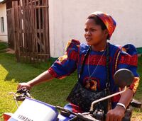 A sister of the Theresienne Sisters of Basankusu wearing a brightly coloured habit, riding a motor-bike, Democratic Republic of Congo, 2013[24]