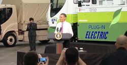 A smiling Barack Obama at a podium in front of an electric truck