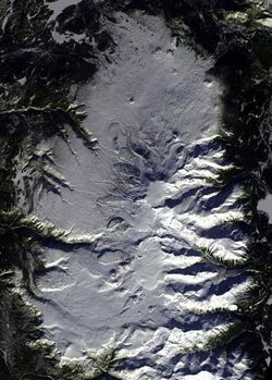 An overhead view of an oval-shaped, snow-covered plateau with a snow-covered mountain in the middle.