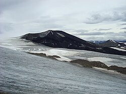 A black cone-shaped mountain rising over glacial ice in the foreground.