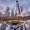 Illuminated water falls into 9/11 Memorial south pool at sunset, and glass-clad One World Trade Center with other skyscrapers in the background