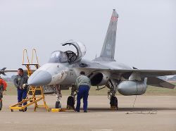 A light fighter aircraft on the ground with two men who are maintaining it.