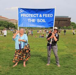 Two climate advocates holding a sign that reads "Protect and feed the soil."