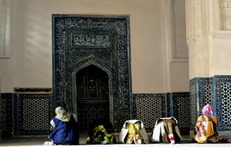 Several women pray inside a building. There is a niche on the wall in whose direction they pray.