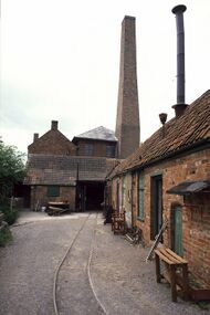 Several red brick buildings and a chimney, with parallel rail tracks in the foreground