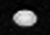 A white oval shaped object somewhat elongated horizontally is seen in the center. There are a few small dark spots on its surface.