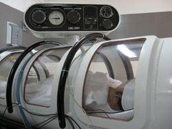 View of the side of a small cylindrical structure with several curved windows and an instrument panel, with a person visible inside